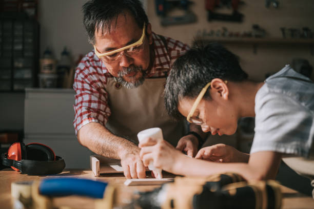 Older craftsperson teaching a young person woodworking in the craft academy